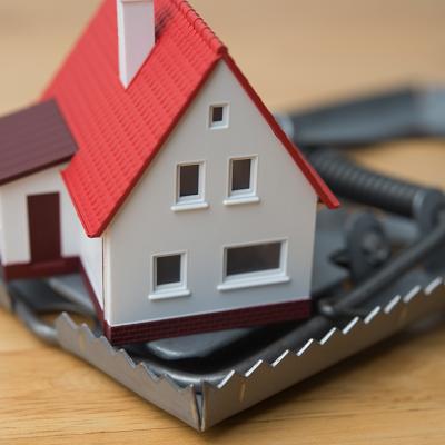 Mortgage scam concept depicted by a figure of a house inside a steel trap.