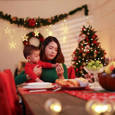 A young mother sitting alone with holding her baby at the dinner table during Christmas Eve.
