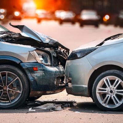 Side view of two silver cars that are stopped in a collision with the hood of one car visibly damaged.