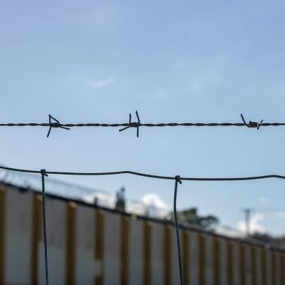 Close up of a single strand of barbed wire above a fence with a correctional facility in the background.