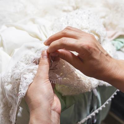 Hands of a seamstress sewing beads on a wedding dress.