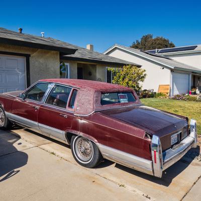 An old red vintage car parked on the driveway of a home.