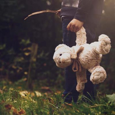 A young boy holding a teddy bear outdoors.