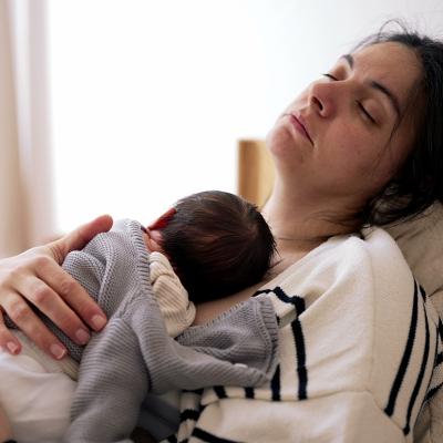 A tired mother sleeping with her newborn on her chest.