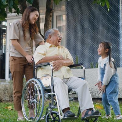 A disabled senior grandfather with his daughter and grandchild in a park.