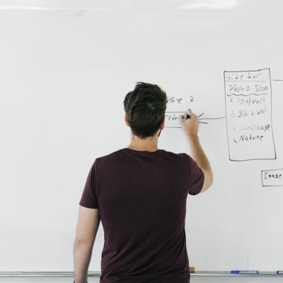 Man writing business planning strategy charts on a wide whiteboard.