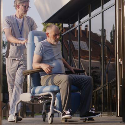 Two doctors assisting a disabled elderly man to the clinic entrance.