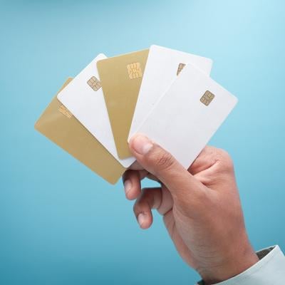 A hand holding an assortment of five gold and white credit card against a blue background.