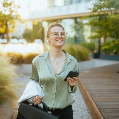 A businesswoman heading to work with a briefcase and listening to wireless earphones.