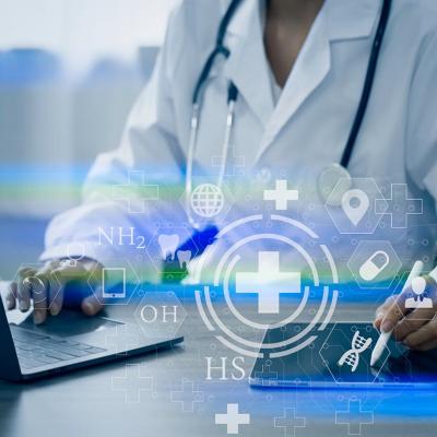 Doctor visible from the neck down sitting at desk with laptop and iPad  working with digital medical interface icons superimposed symbolizing AI. 