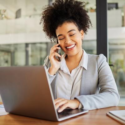 A businesswoman in conversation with someone on her phone and working with a laptop in an office.