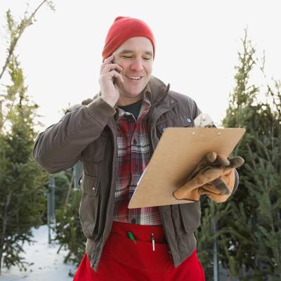 A man talking with someone on the phone while working outdoors for a Christmas tree shop.