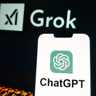 A smartphone displaying the ChatGPT logo and a laptop screen displaying X's Grok logo in the background.