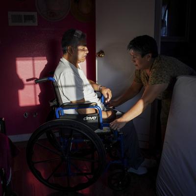 Maria Patricia Alcantara (R), wheels Jose Epifanio Sanchez Trujeque (L) to the bathroom at their home in Lebec, California.