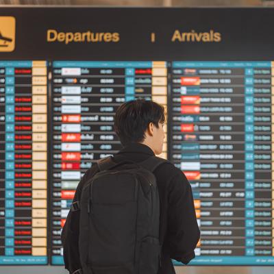 Rear view of a young man with a backpack looking at an airport's flight schedule board.