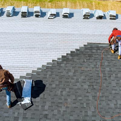 Aerial view of roof workers installing shingles using hammer and nail.