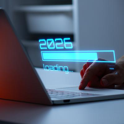 A person's hand interacting with a laptop illustrated with a holographic '2026 loading' graphic.