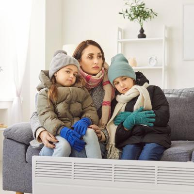 A mother with her two children in winter clothing sitting on a sofa in a cold living room.