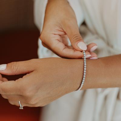 A bride putting on an elegant bracelet on her left wrist.