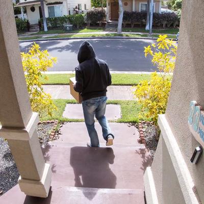 A surveillance camera-view of a package thief walking away from a porch after taking a package.