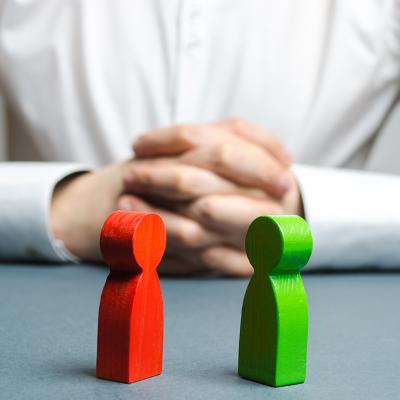 An arbitrator visualizing conflict situation between people depicted by two wooden figures.