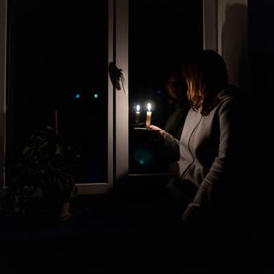 A woman standing by the window holding a candle during a power outage.