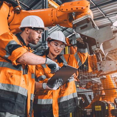 Two members of an engineering team looking at programming in a tablet inside their automated manufacturing factory.