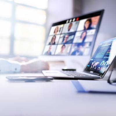 An employee's laptops at work displaying dashboards and a virtual video call.