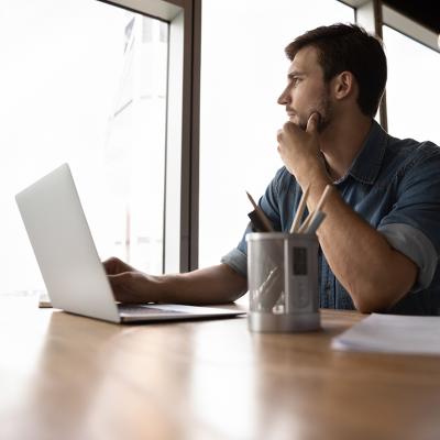 A male professional looking out the office window, pondering on work decisions.