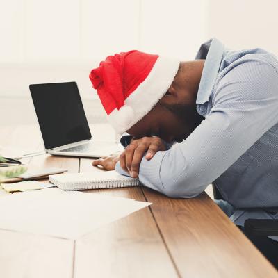 A tired businessman wearing a Christmas hat while asleep at work.