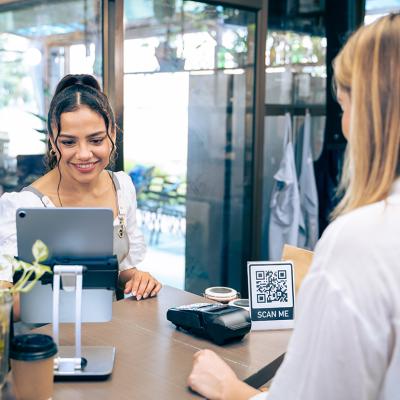 Barista receives a customer lining up to pay in a cafe's counter where a QR code information graphic is displayed.