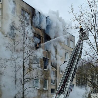 A firefighter on a lift sprays water from a hose into an apartment building as smoke pours out.. 