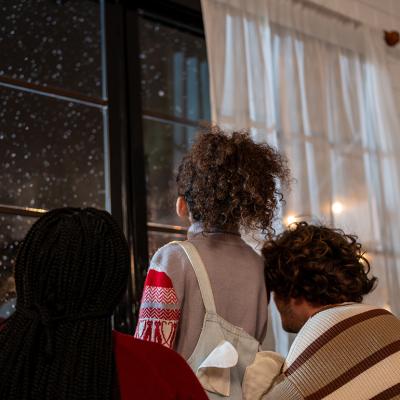 A family looking at the window to see snowfall at night.