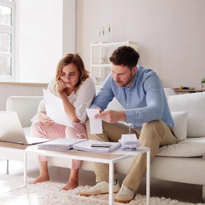 Two people sitting on a white sofa looking at bills and paperwork in a minimalistic living room.