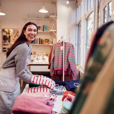 A female business owner arranging stock clothing for her store's window display.