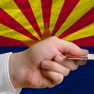 A person's hand holding a credit card with a background of Arizona's flag.