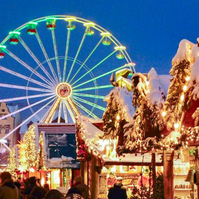 A ferris wheel lights up the night sky during twilight at the Erfurt Christmas Market with vendors selling festive goods in the foreground.