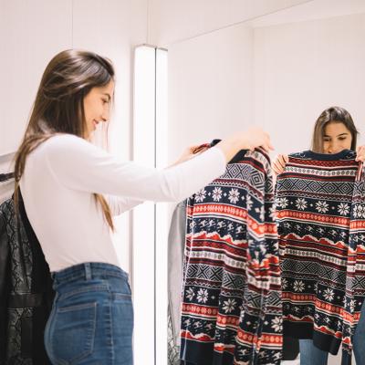 A young woman looking at a winter sweater in a dressing room.