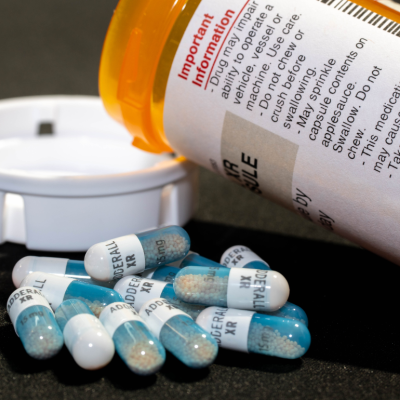 Closeup of an open bottle of adderral medication with some pills laying next to the bottle.