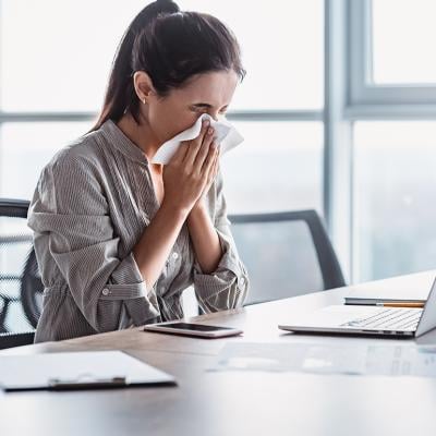 A sick businesswoman blowing her nose at work.