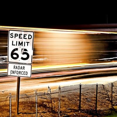 65 mph speed limit sign with a background of long exposure trails.