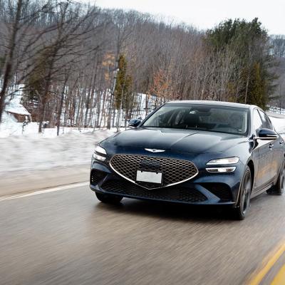 Front view of black Genesis G70 driving on a road in winter with snow and trees in background. 