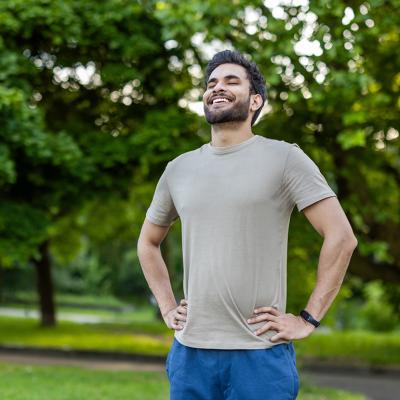 A sporty young man standing outdoors with hands on hips, smiling after an exercise.
