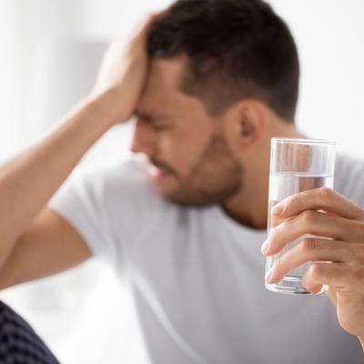 Man experiencing hangover holding a glass of water.