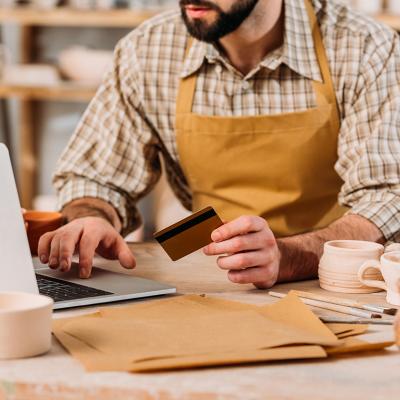 Cropped view of a small pottery business owner holding a credit card and browsing a laptop.