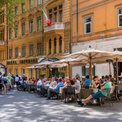 Tables under umbrellas filled with people outside of restaurants in Rome. 