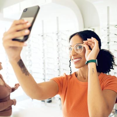 A young woman trying on eyeglasses in a shop and taking a selfie.