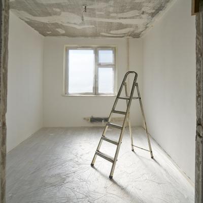 A ladder at the center of an apartment room with unfinished interior paint. 