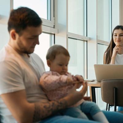 Woman smiling and sitting at table with laptop looking at man holding baby in the foreground.