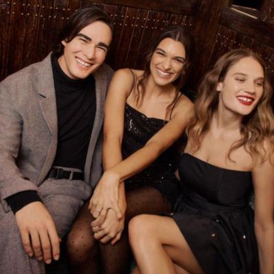 A group of three young personalities happily posing and sitting on an events sofa during a holiday celebration.